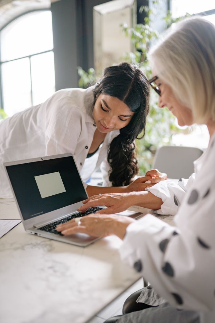 Two women in a modern office collaborate over a laptop, fostering teamwork and innovation.